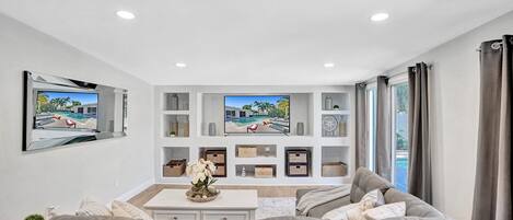 A modern living room with a grey sofa, a coffee table with a floral centerpiece, and a TV mounted on the wall.