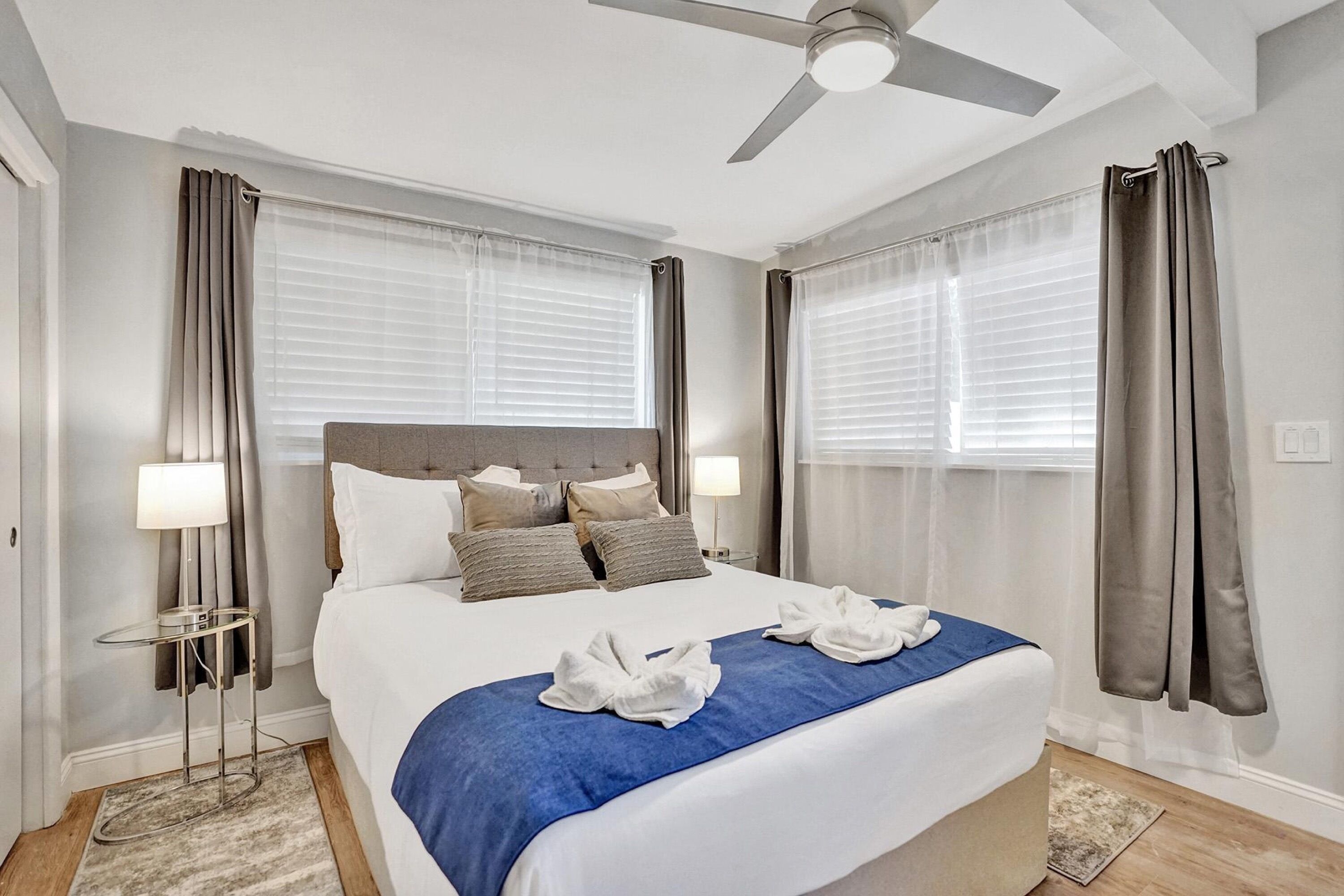 A neatly arranged hotel room with a bed, a ceiling fan, and a nightstand with a lamp.