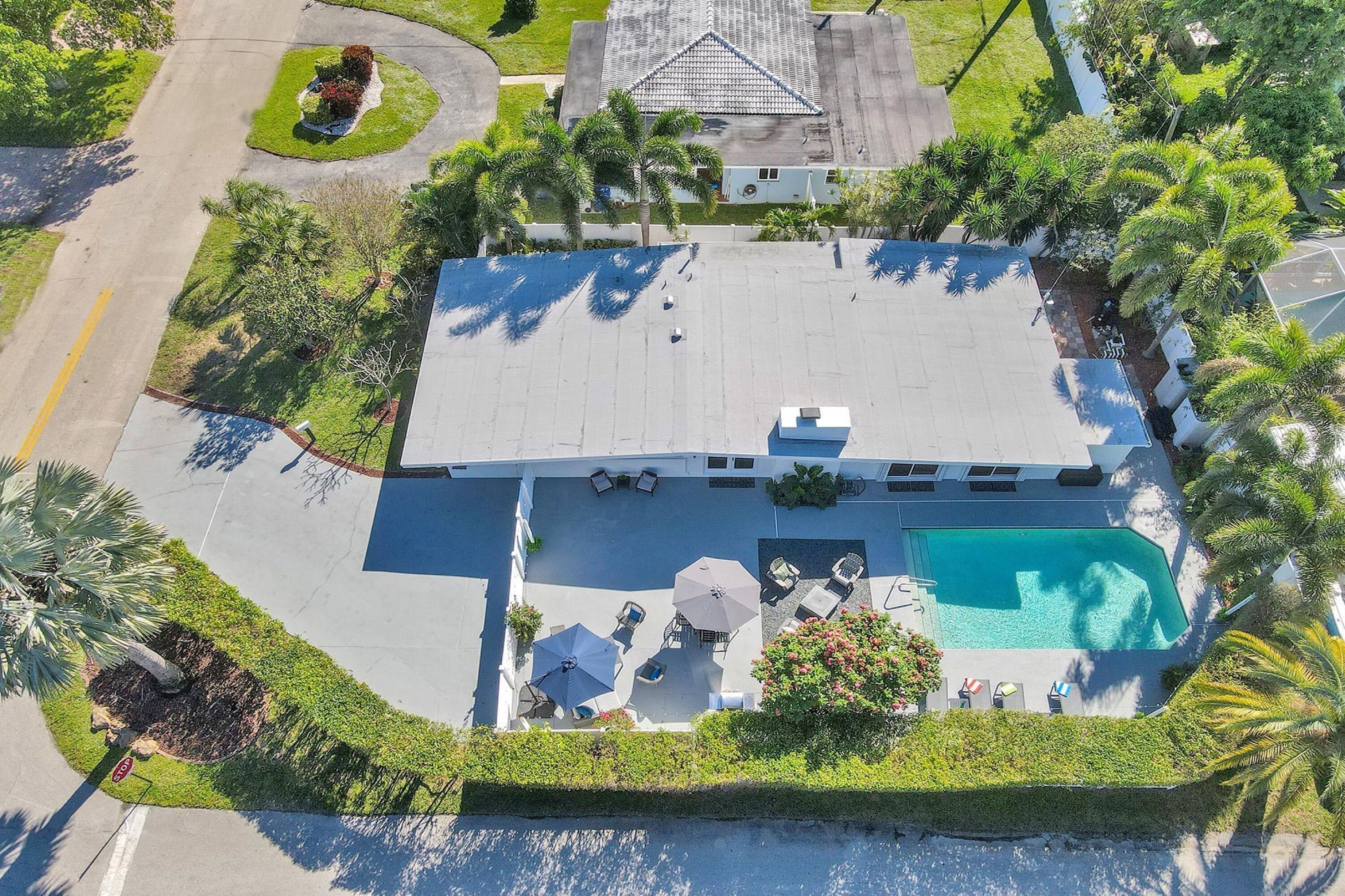 Une vue aérienne d’une maison avec une piscine, entourée d’une végétation luxuriante et de palmiers.