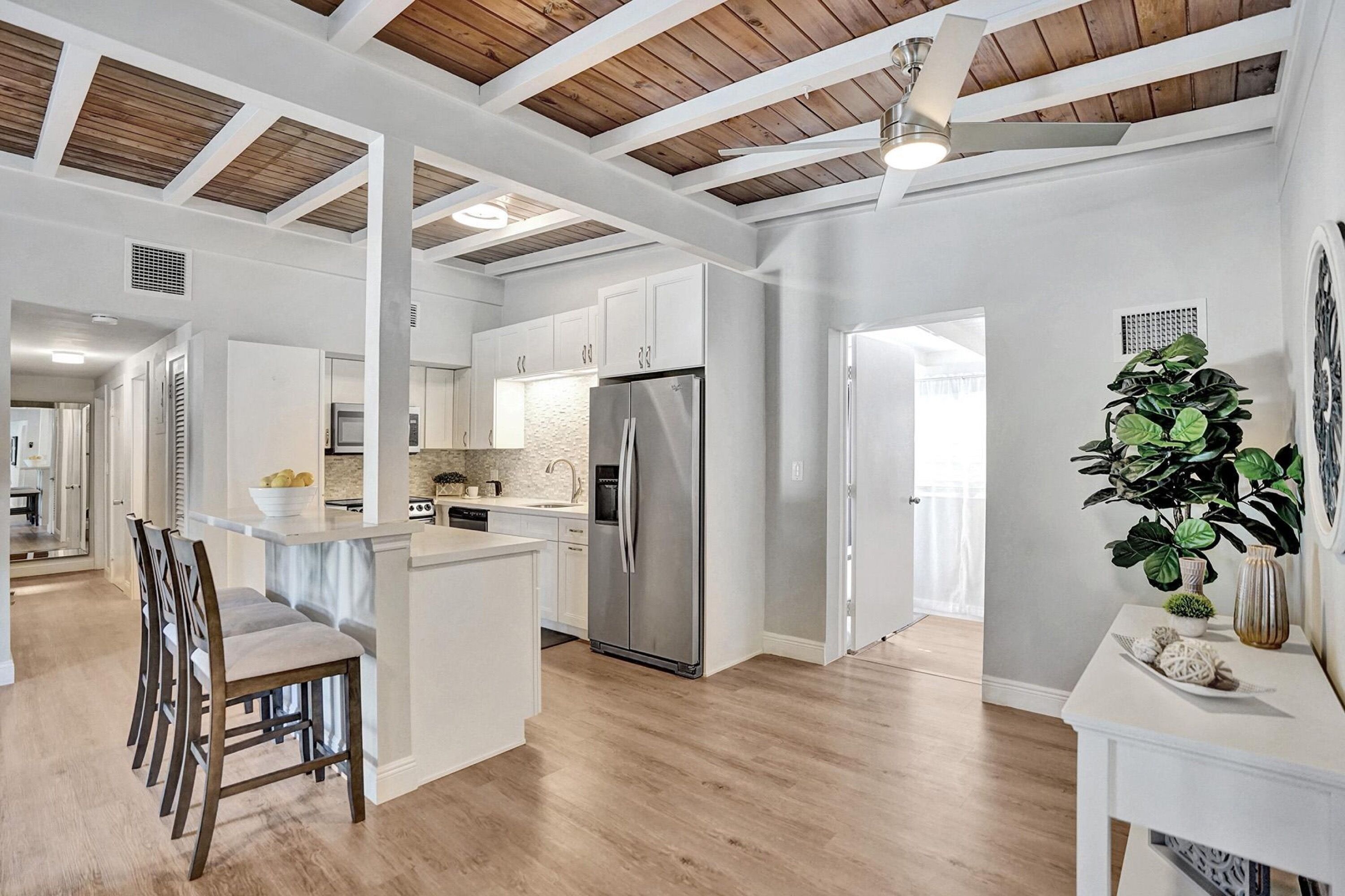 A spacious kitchen with a central island, wooden beams on the ceiling, and a large refrigerator.