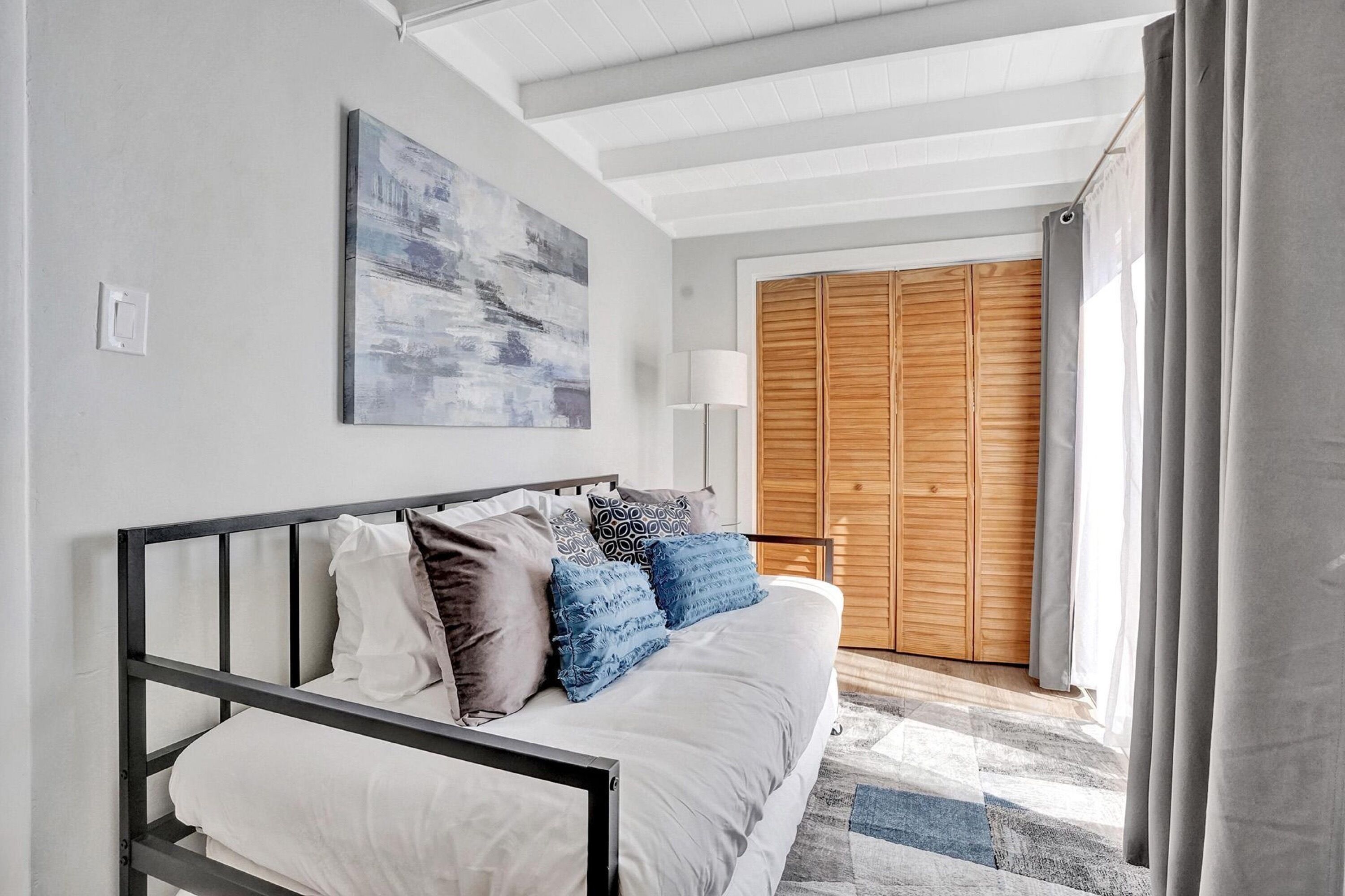 A bedroom with a bed, a painting, a wooden wardrobe, and a lamp.