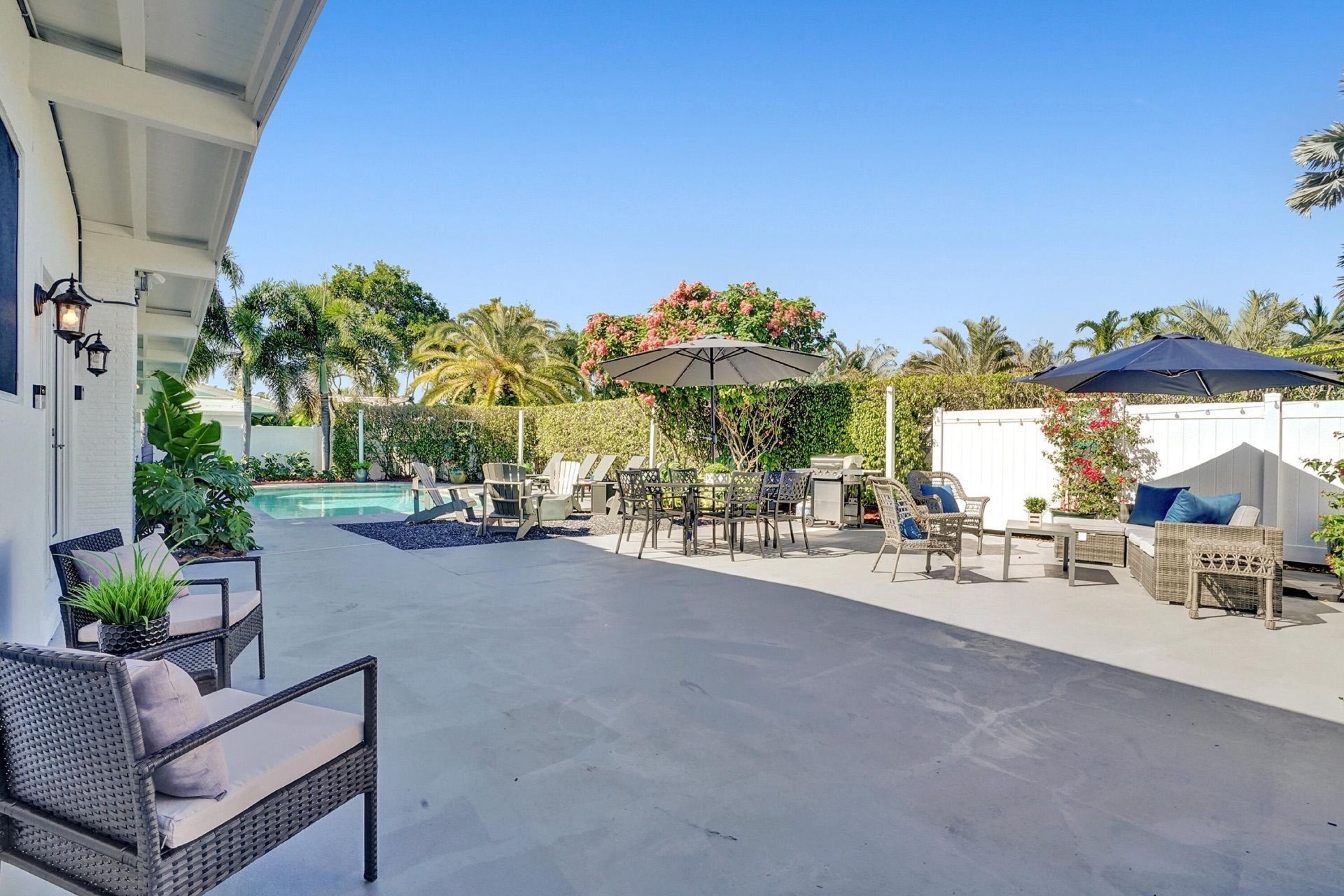 An outdoor patio with wicker furniture, a pool, and a covered area with umbrellas.