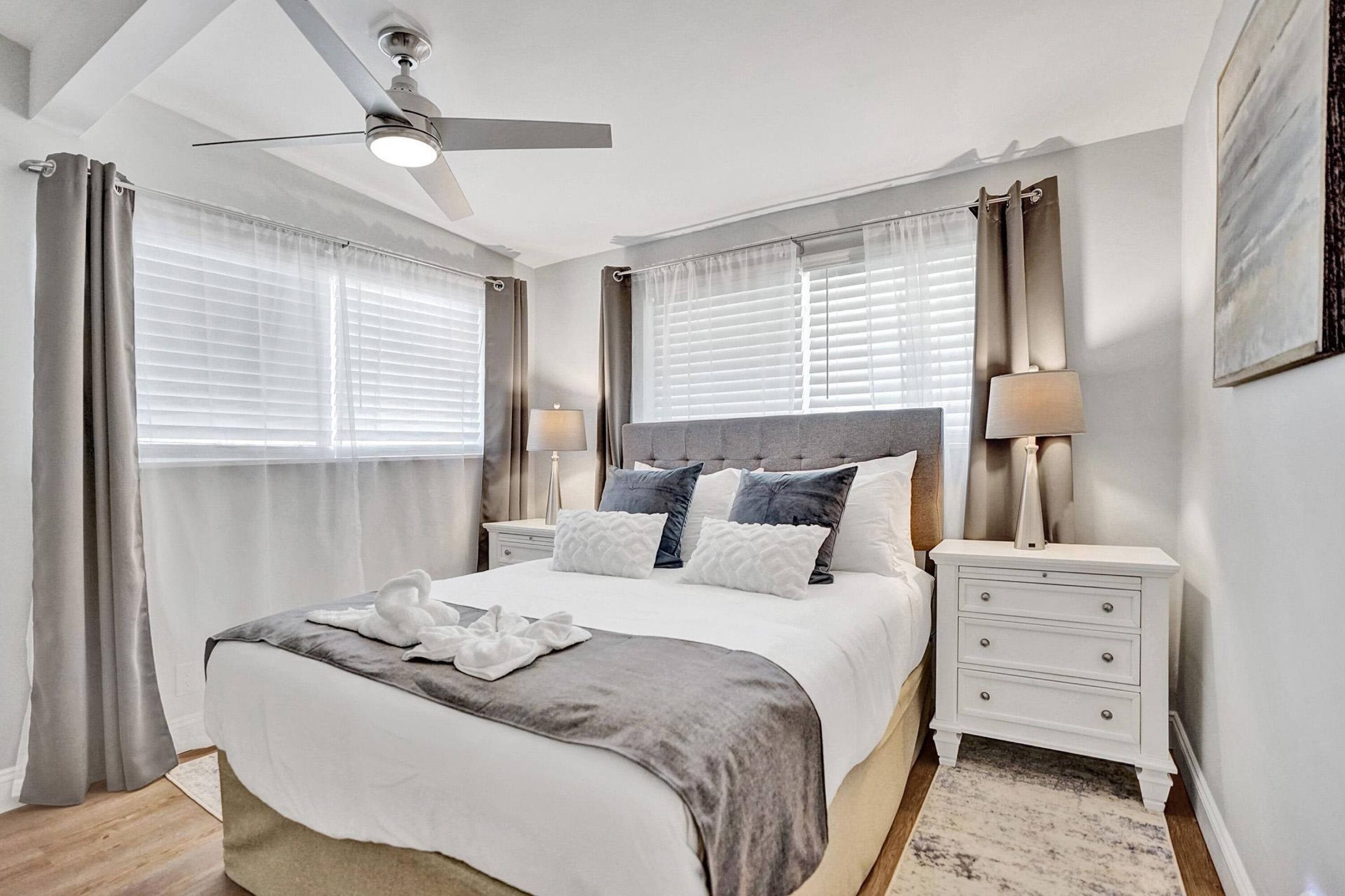 A modern bedroom with a bed, nightstands, a ceiling fan, and a window with curtains.