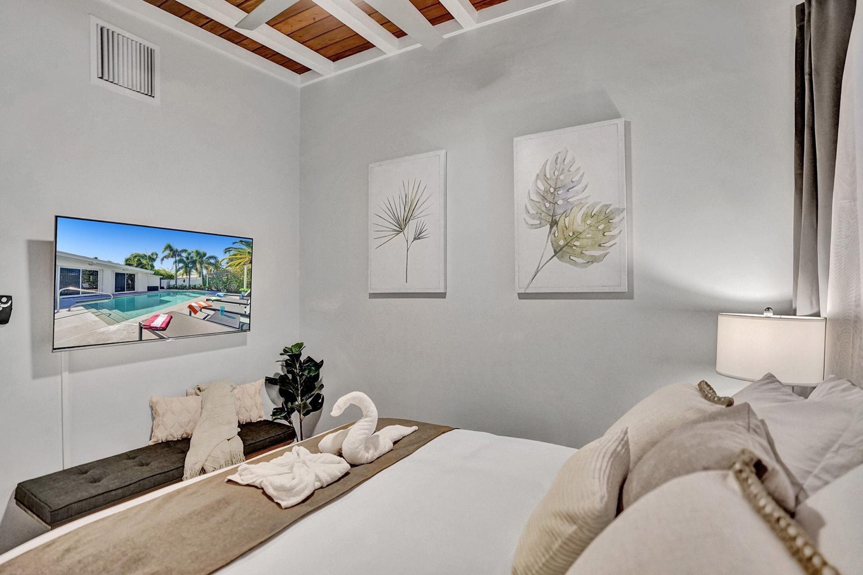 Een hotelkamer met een bed, een televisie waarop een uitzicht op het zwembad te zien is, en wanddecoratie.