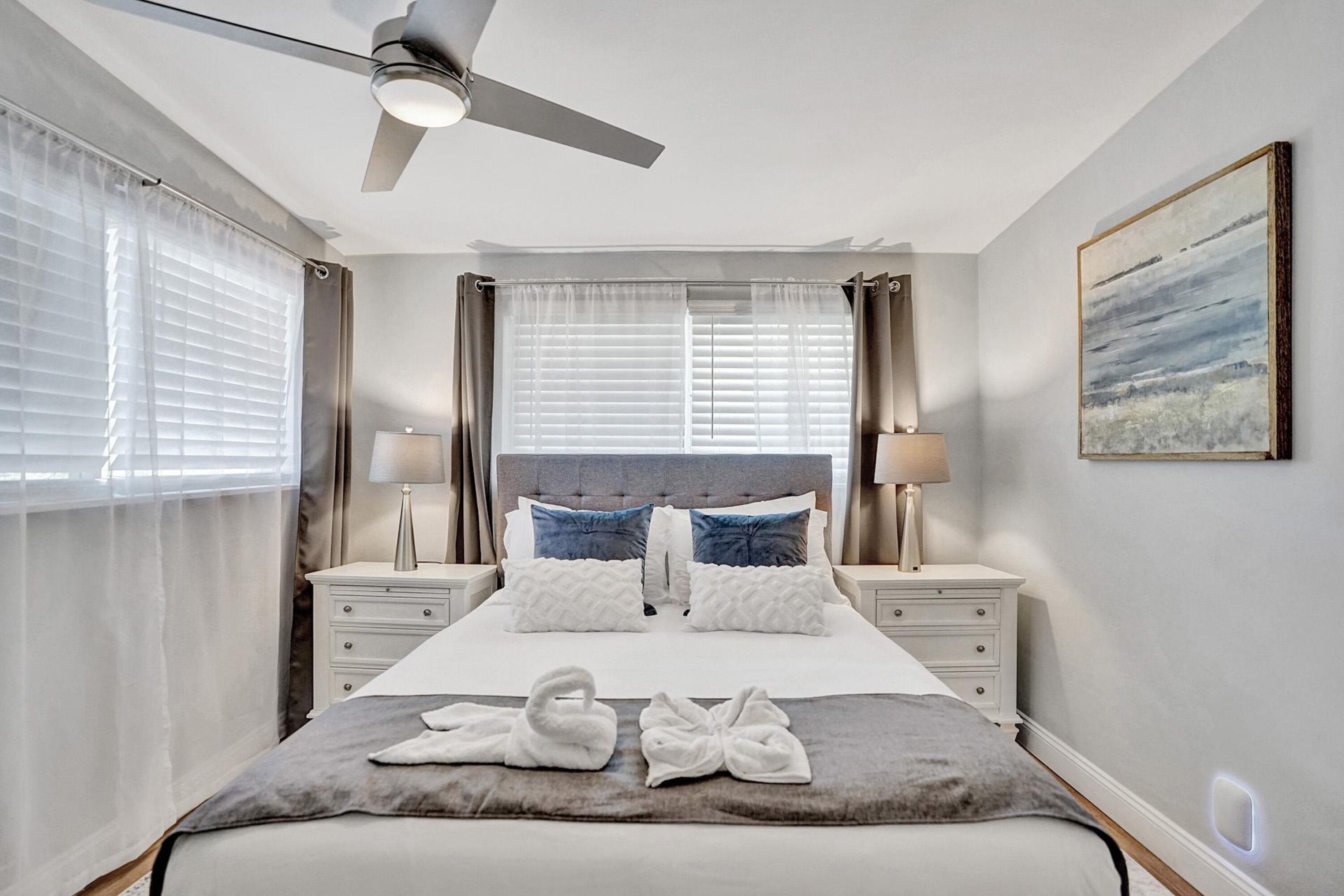A neatly arranged hotel room with a large bed, two bedside tables, a ceiling fan, and a painting on the wall.