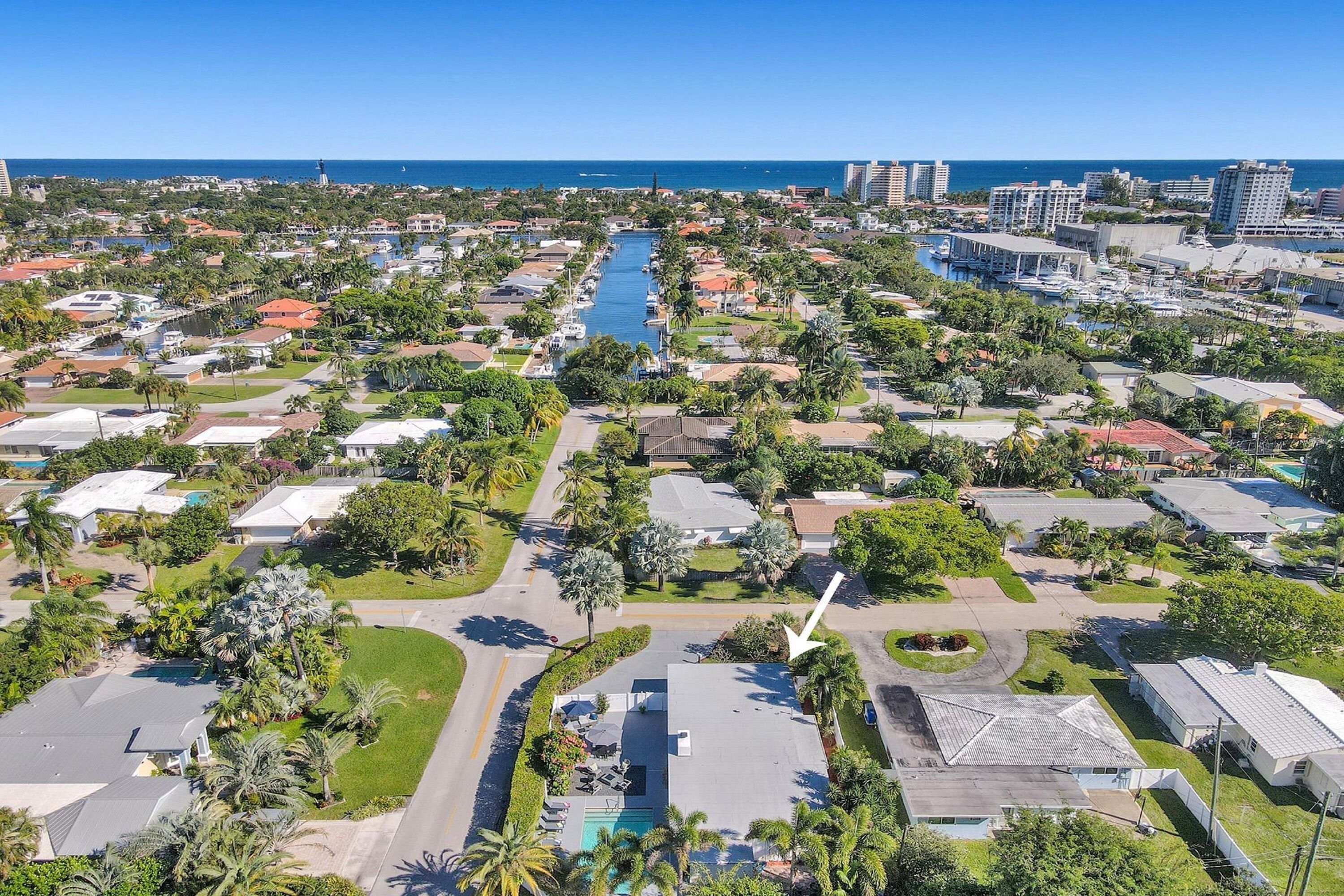 An aerial view of a coastal residential area with a central waterway, surrounded by single-family homes, some with visible swimming pools.
