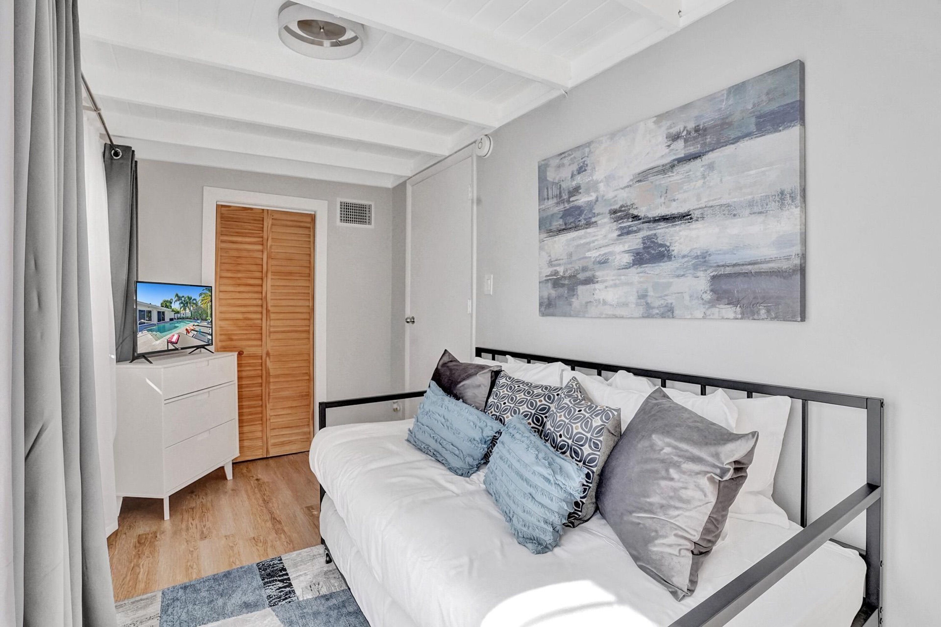 A modern bedroom with a bed, a TV on a dresser, and a large abstract painting on the wall.