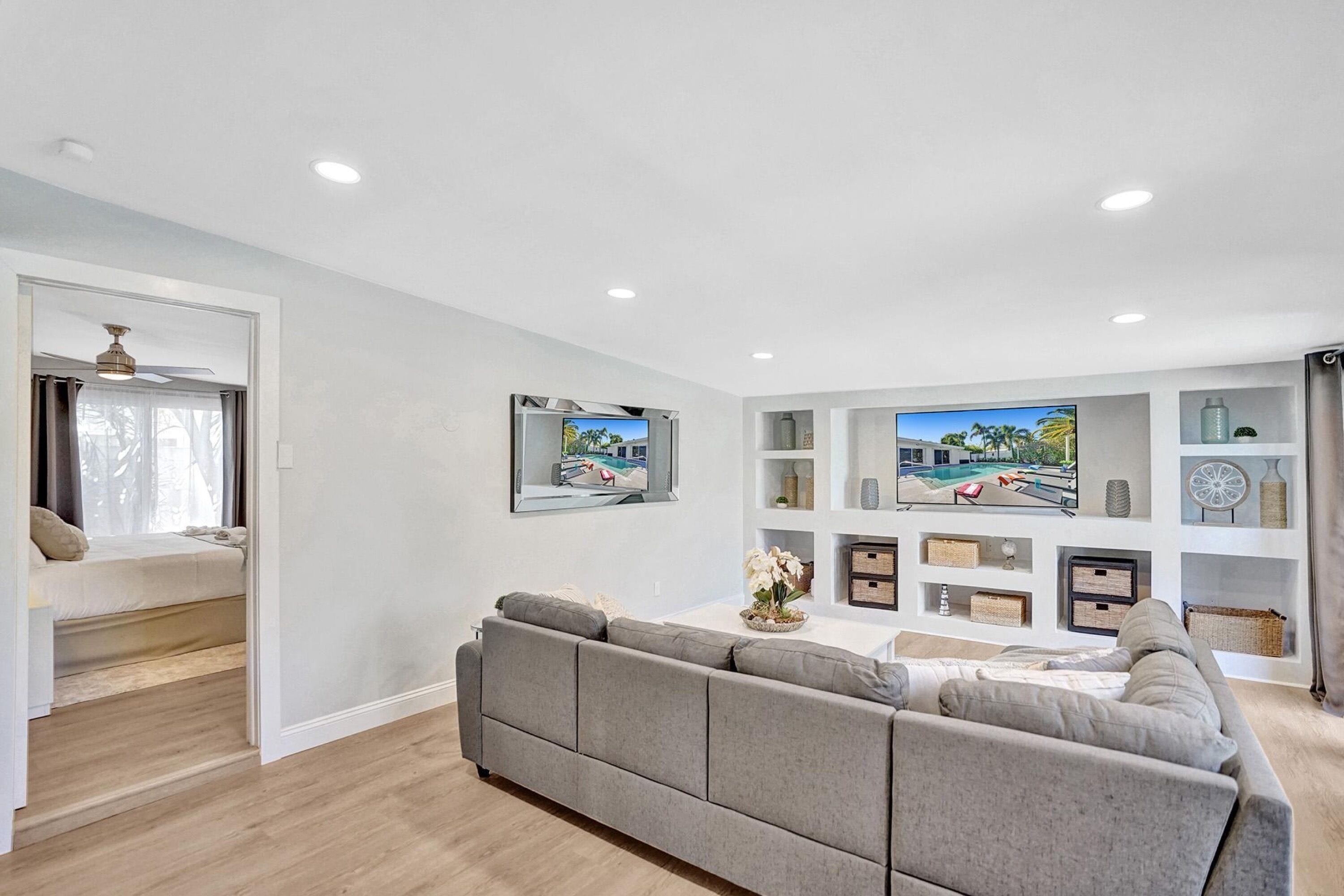 A modern living room with a grey sectional sofa, a flat-screen TV mounted on the wall, and built-in shelving with decorative items.