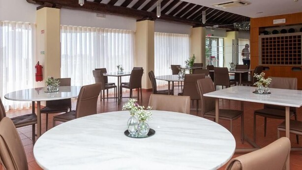 Un restaurante con mesas redondas y rectangulares, algunas con centros de mesa florales.