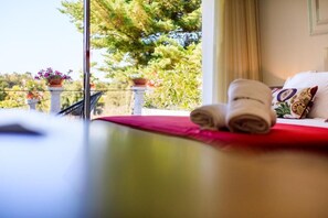 A hotel room with a balcony, a bed with a red bedspread, and a view of greenery and trees. - Hotel Campo do Rosmaninho (Castelo Branco)