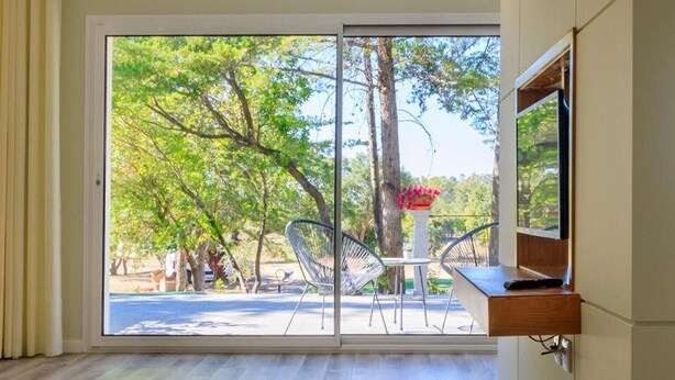 A room with a sliding glass door leading to a patio with outdoor furniture and trees. - Hotel Campo do Rosmaninho (Castelo Branco)