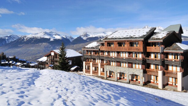 Un hotel de diverses plantes amb un teulat cobert de neu, ubicat en una zona muntanyosa amb el terreny nevado.