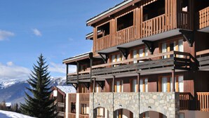 Un edifici de fusta de diverses plantes amb balcons, arcs de pedra i un paisatge nevós al fons.