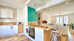 A modern kitchen with a central island, wooden cabinets, and a teal accent wall. - Renovated T3 Apt with Balcony & Parking in Annecy Center (Annecy)
