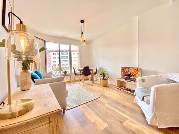 Uma sala de estar moderna com uma mesa de centro de madeira, um sofá, uma TV e uma área de jantar com cadeiras e uma pequena mesa.