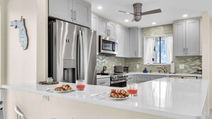 Une cuisine moderne dotée d’appareils électroménagers en acier inoxydable, d’un grand îlot central et d’un ventilateur de plafond.