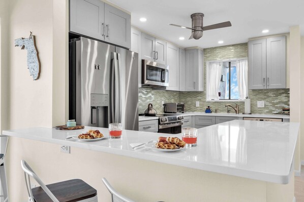 A modern kitchen with stainless steel appliances, a large island, and a ceiling fan.