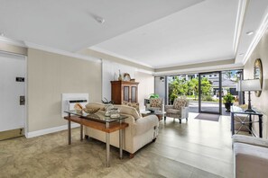 A spacious living room with a sofa, coffee table, and armchairs. A dining area with a table and chairs is visible in the background.