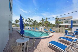 A pool area with lounge chairs and umbrellas, surrounded by palm trees and a white fence.