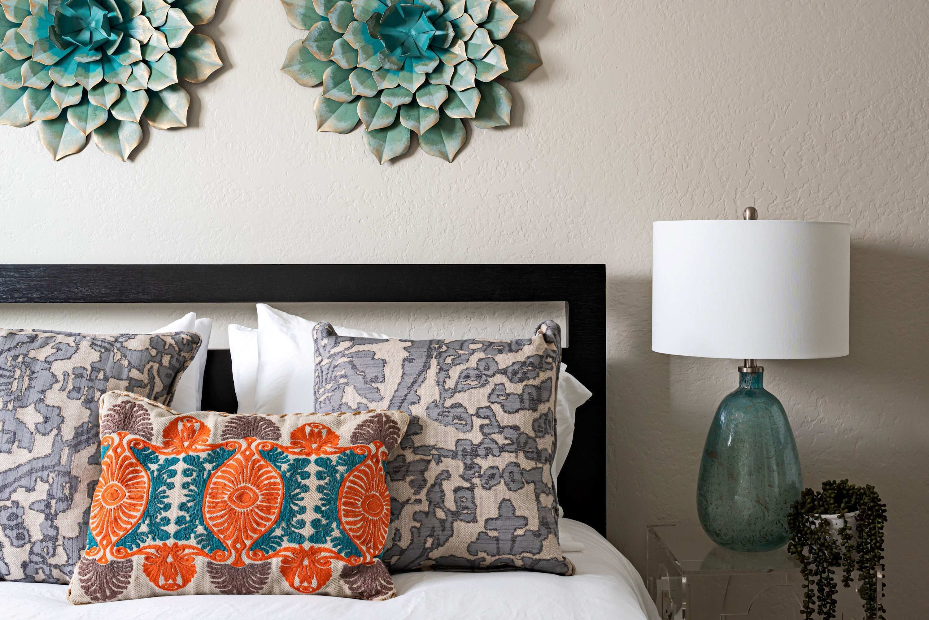A bed with patterned pillows, a wall-mounted decorative piece, and a lamp.