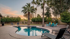 A swimming pool with lounge chairs and a fire pit area, surrounded by palm trees and a brick patio. - Art Deco Oasis: Vintage Charm, Pool, Firepit, BBQ (Scottsdale)