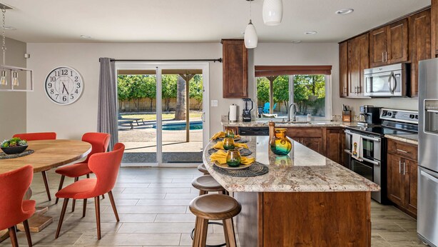 A modern kitchen with a central island, stainless steel appliances, and a dining area with red chairs. - Art Deco Oasis: Vintage Charm, Pool, Firepit, BBQ (Scottsdale)