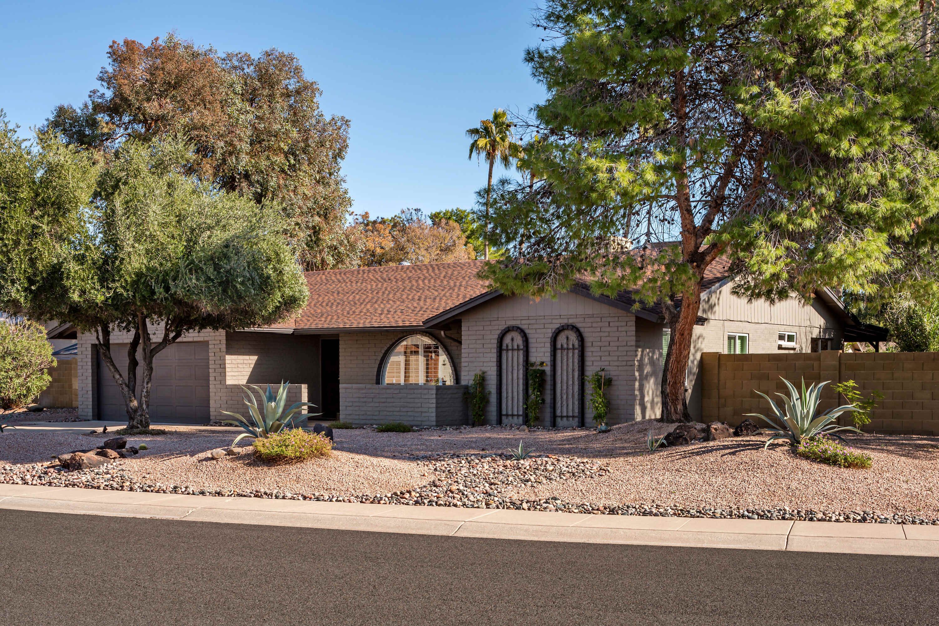 A residential house with a brick exterior, a garage, and a landscaped front yard with trees and shrubs.
