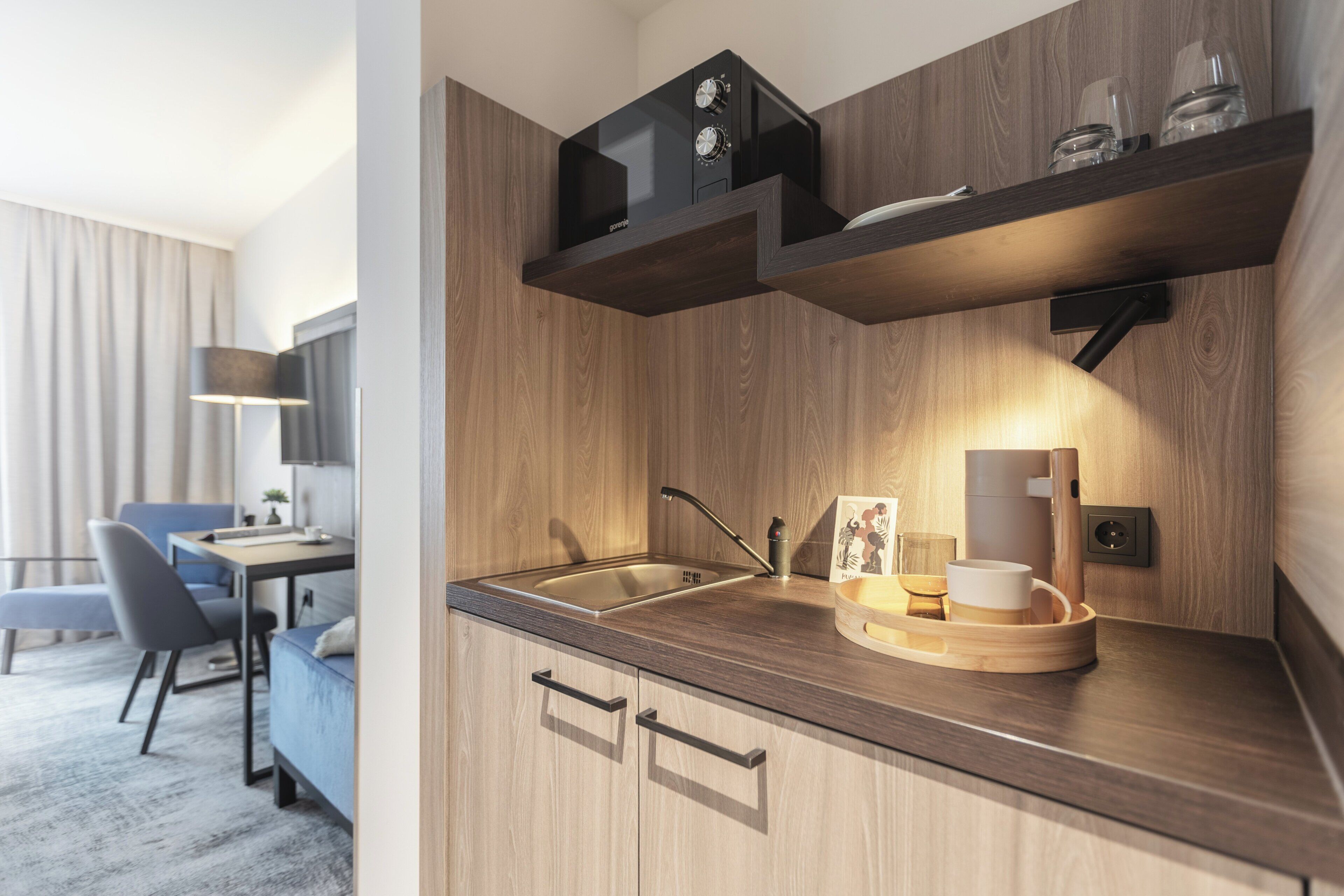 Eine moderne Küche mit Holzausbau, einer Edelstahlspüle und einem Einbauofen. Es gibt einen Essbereich mit Tisch und Stühlen, und eine Lampe steht daneben.