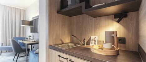 Una cocina moderna con armarios de madera, un lavamanos de acero inoxidable y un horno empotrado. Hay un comedor con una mesa y sillas, y una lámpara al lado.