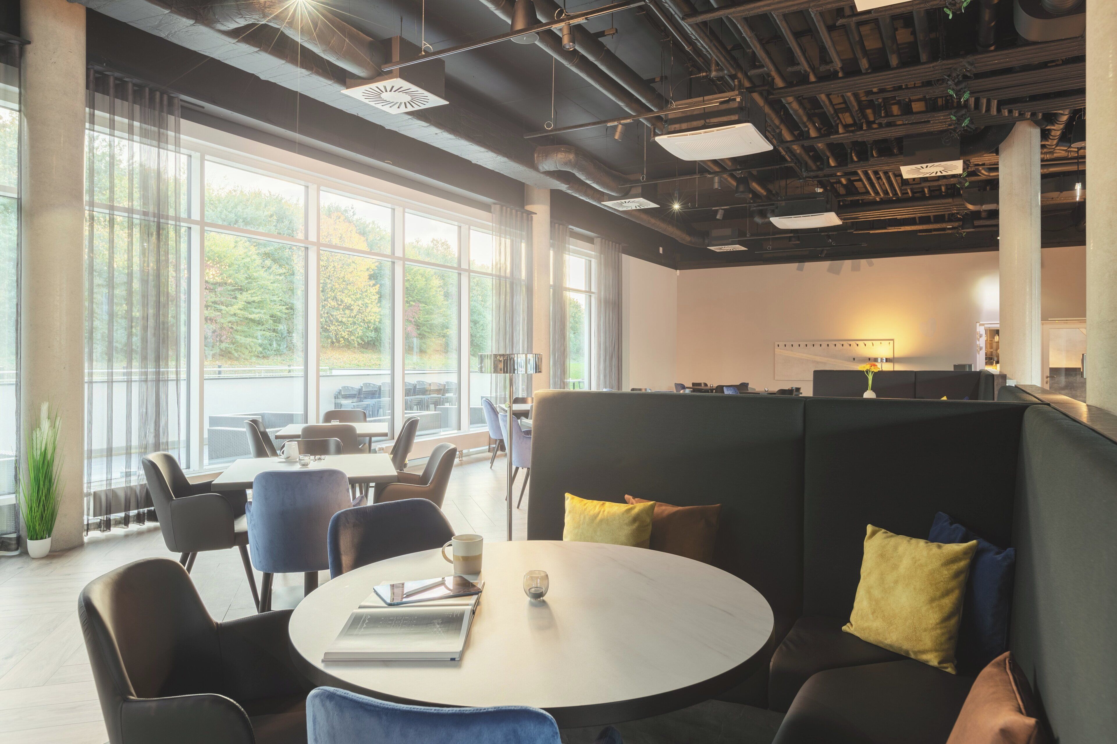 A modern office space with round tables, comfortable seating, and large windows offering a view of the outdoors.