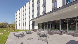 An outdoor patio area with multiple seating arrangements, including tables and chairs, and a large glass wall providing views of the surrounding area. - Candlewood Suites Augsburg by IHG (Gersthofen)