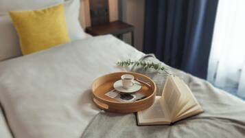 Ein ordentlich bezogenes Bett mit einem Tablett, das eine Tasse und ein Buch hält, einer Nachttischlampe und einem Fenster mit Vorhängen.