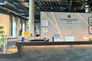 A reception desk with a sign for Candlewood Suites by IHG, a glass display case with snacks, and a digital payment terminal. - Candlewood Suites Augsburg by IHG (Gersthofen)
