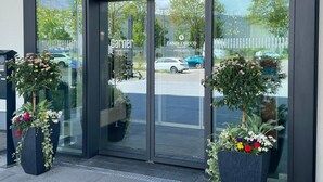 A hotel entrance with glass doors, a sign for 'Garnier Hotel', and two large flower planters. - Candlewood Suites Augsburg by IHG (Gersthofen)