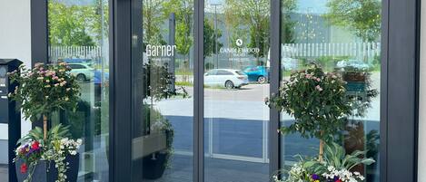 Entrada de un hotel con puertas de vidrio, un letrero que dice 'Garnier Hotel' y dos grandes macetas con flores.