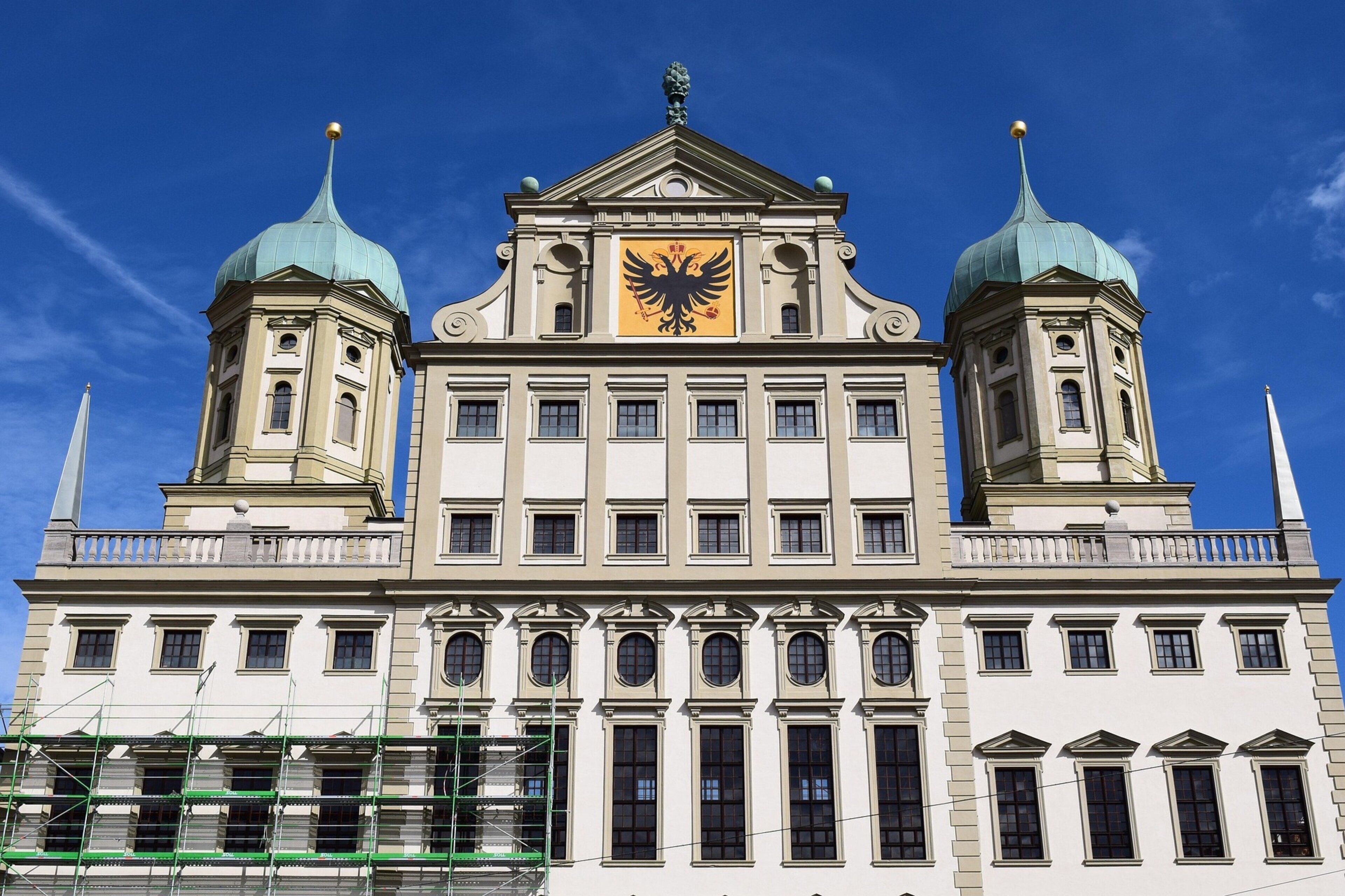 A large building with two green domed towers and a central golden eagle emblem.