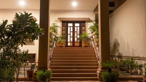 A grand staircase with a wooden finish, flanked by large columns and potted plants, leading to a wooden door at the top. - Hanuwant Niwas (Jodhpur)