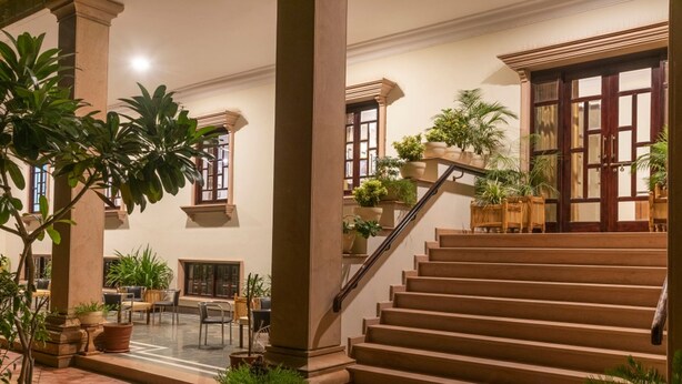 A spacious indoor area with a staircase, columns, and potted plants. - Hanuwant Niwas (Jodhpur)