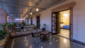 A spacious lobby with a high ceiling, potted plants, a wooden table, and a bed visible through an open doorway. - Hanuwant Niwas (Jodhpur)