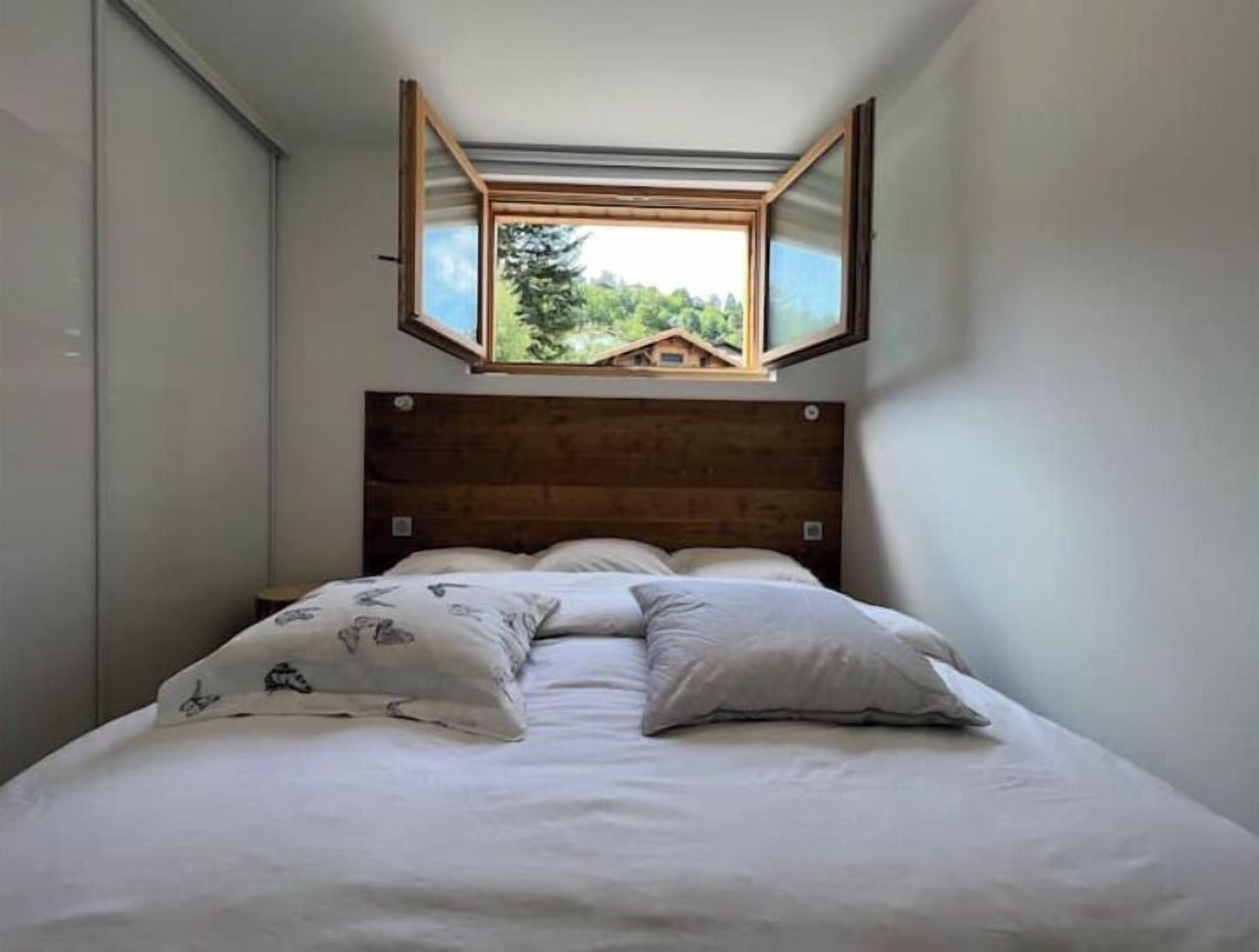 Un dormitorio con cabecera de madera, cama con ropa blanca y un tragaluz sobre la cama.