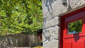 A stone exterior wall with a red door, a wooden table and chairs, and a metal fence.
