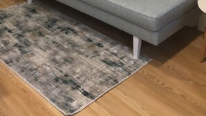 A grey sofa with a patterned rug in front of a white vertical blinds wall.
