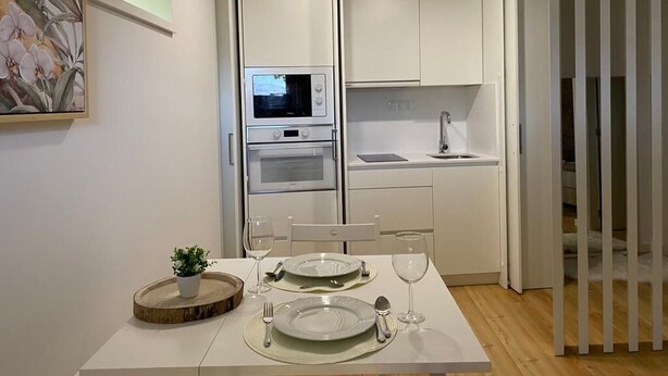 A compact kitchen with white cabinets, a microwave, and a sink. There is a dining table set with plates, cutlery, and glasses.