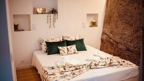 A neatly made bed with floral bedding, two green pillows, and a decorative wall shelf with a heart-shaped sign.
