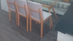 Uma sala de jantar moderna com mesa de vidro e cadeiras de madeira, um sofá com almofadas amarelas, e uma cozinha com bancada de mármore e armários.