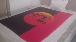 Uma cama com cabeceira branca e manta colorida com desenho de dragão.