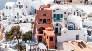 A coastal town with white buildings, a prominent red-roofed structure, and a clear view of the sea. - Terracotta Cave House (1) (Santorini)