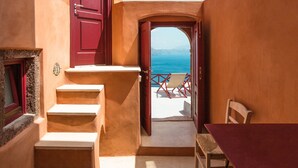 A room with a red door, a staircase, a table, and a view of the sea. - Terracotta Cave House (1) (Santorini)