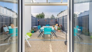 Eine moderne Terrassenanlage im Freien mit Glaswand, Tisch und Stühlen sowie Pflanzen in Töpfen.