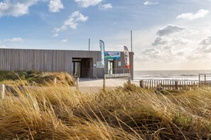 A modern building with a wooden facade near the beach, featuring a signboard and flags. - 3-bedroom house, 250 m from the beach in the Vendée (Saint-Hilaire-de-Riez)